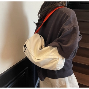 Detail of cream nylon pillow bag with bright orange strap worn by model on stairs