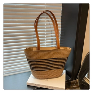 Detail of woven straw bucket bag featuring horizontal black stripes and leather straps