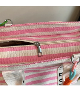 Detail view of pink and white striped canvas bag showing metal zipper and colorful woven rope