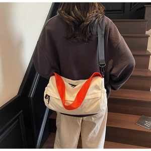 Detail of white canvas crossbody bag with vibrant orange wide shoulder strap on model