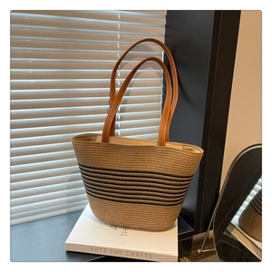 Detail of straw tote bag with black stripes and brown leather handles on books