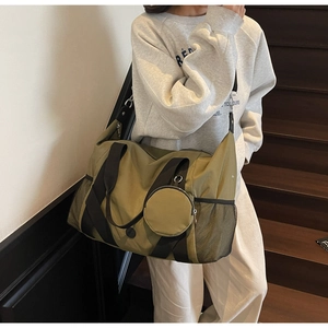 Olivgrüne Reisetasche mit schwarzen Gurten und Rundetui an einem Modell bei Treppen
