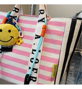 Detail of pink striped canvas tote bag with woven logo straps and yellow smiley charm