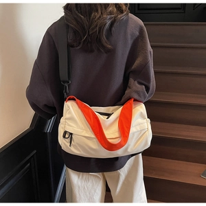 Close-up of a white crescent messenger bag with a vibrant orange crossbody strap on a model