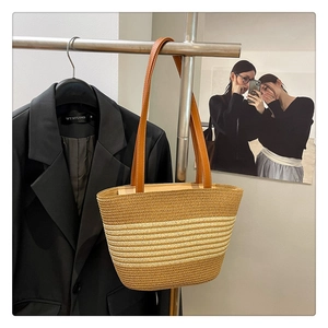 Detail of woven straw tote bag featuring brown leather handles and striped texture
