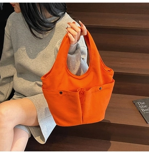 Close-up of orange canvas tote bag showing double front pockets with metal snaps