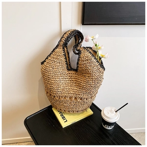 Detail of handcrafted straw tote bag with black contrast trim and hollow weave details