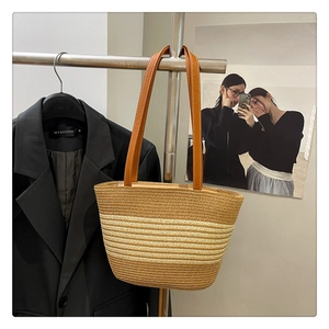 Detail of a striped woven straw tote bag with brown leather handles on a hanger