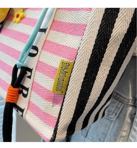 Close-up of colorful striped canvas tote bag with yellow flower charm and blue drawstring detail