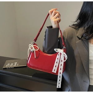 Dettaglio borsa in pelle lucida rossa con fiocco in pizzo bianco e ciondolo di perle