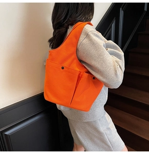 Bright orange pleated canvas tote bag with double front pockets worn by a model