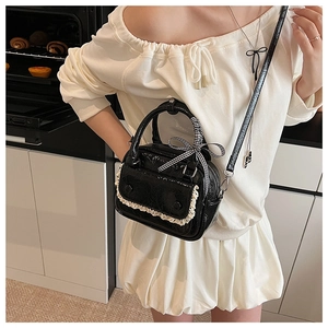 Close-up of black patent leather handbag with white lace trim and checkered bow detail