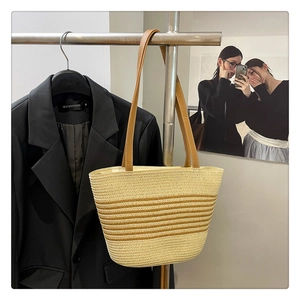 Detail of hand-woven straw tote bag with brown stripes and leather shoulder straps