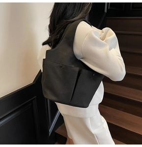 Detailed side view of a minimalist black canvas tote bag with dual front pockets on a model