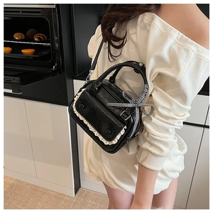 Detail of black crossbody bag with white lace trim and checkered bow in home setting