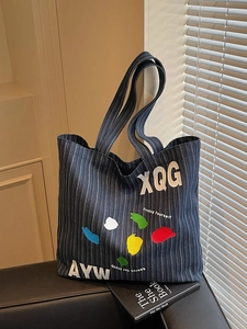 Large denim tote bag with blue stripes and artistic colorful prints on a black sofa