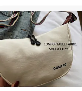 Detail of off-white canvas crescent bag with black OOMTAO logo and striped wide shoulder strap