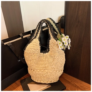 Detail view of woven straw tote bag with black contrast handles on dark wood surface