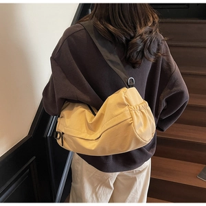 Detail of a cream nylon crescent bag with ruching, black strap and D-ring on wood stairs