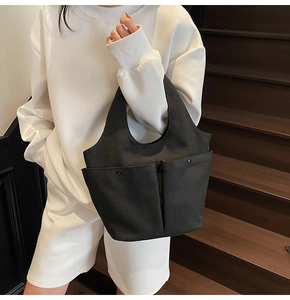 Detailed close-up of double front pockets with snap buttons on a black canvas tote bag