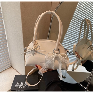 Dettaglio borsa beige con fiocco, ciondolo in pizzo perlato e texture in pelle pregiata