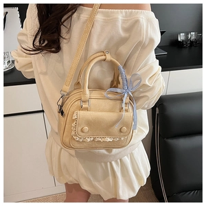 Detail of cream yellow Boston bag with lace trim, blue plaid bow and pleated texture