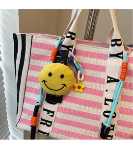 Detail of pink and white striped canvas tote bag with woven handles and a yellow smiley charm