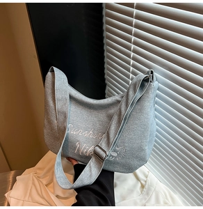 Détail du sac hobo en denim bleu clair avec broderie blanche et bandoulière réglable