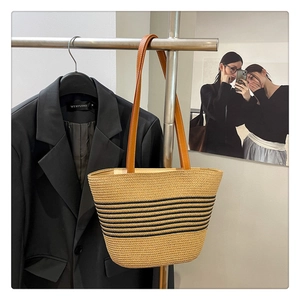 Detail of woven straw bucket bag with black stripes and brown leather handles