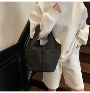 Close-up of black canvas tote bag with dual front pockets and metal rivet details