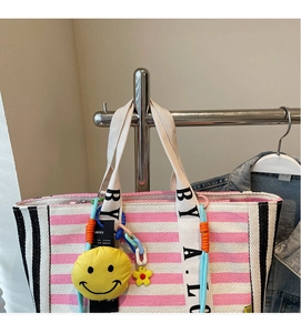 Detail of pink striped canvas tote bag with yellow smiley charm and lettered handles