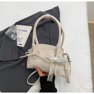 Dettaglio borsa a mano crema con fiocco di perle e pizzo su sfondo grigio