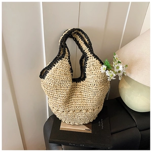 Detailed view of handmade woven straw tote bag with black crochet handles on book