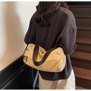 Detail of a large khaki crossbody bag with black wide straps on a model in a stair setting