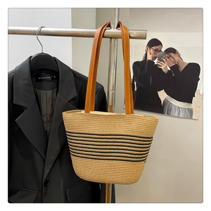 Detail of hand-woven straw tote bag with black stripes and brown leather straps