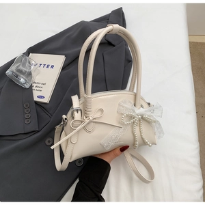 Dettaglio borsa beige a conchiglia con fiocco in pizzo e nappine di perle eleganti