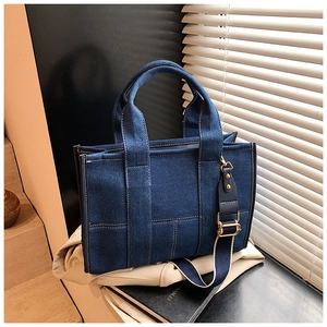 Close-up of dark blue denim tote bag with white stitching and gold metal hardware