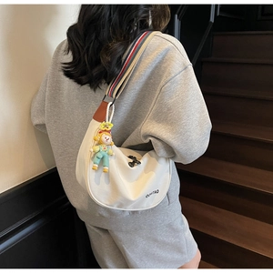 Detail of white dumpling bag with colorful striped strap and cartoon charm shown on model