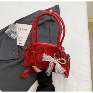 Dettaglio borsa a fiocco rossa con pendente in perle e pizzo su abito grigio