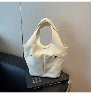 Detail view of cream canvas tote bag featuring double front pockets and metal rivet accents