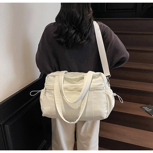 Detail of a beige nylon travel bag with adjustable strap and side drawstring pockets