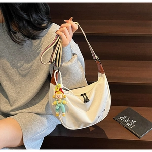 Detail of white canvas crescent bag featuring vibrant striped strap and cartoon doll charm