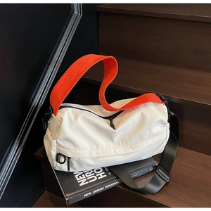 Close-up of cream crossbody bag with bright orange handle on modern stairs