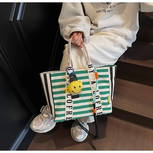 Close-up of green striped canvas tote with yellow plush smiley charm and brand strap