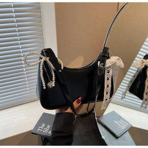 Dettaglio borsa hobo nera con ciondolo a fiocco di perle e fiocco in pizzo bianco