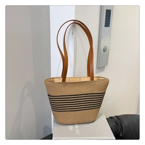 Close-up of woven straw tote bag featuring black stripes and brown leather handles
