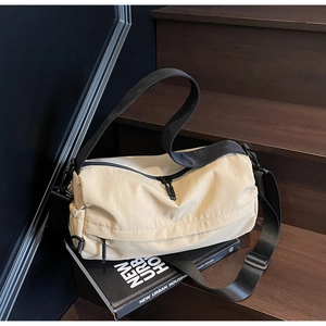 Detail view of cream nylon sports crossbody bag with black straps on an urban style book