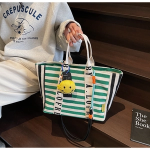 Detail of green striped canvas tote bag with a yellow plush smiley face charm