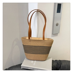 Detail of woven straw bucket bag showing brown leather handles and black stripe pattern