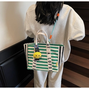 Detailed close-up of green and white striped tote bag with lettered straps and smiley charm